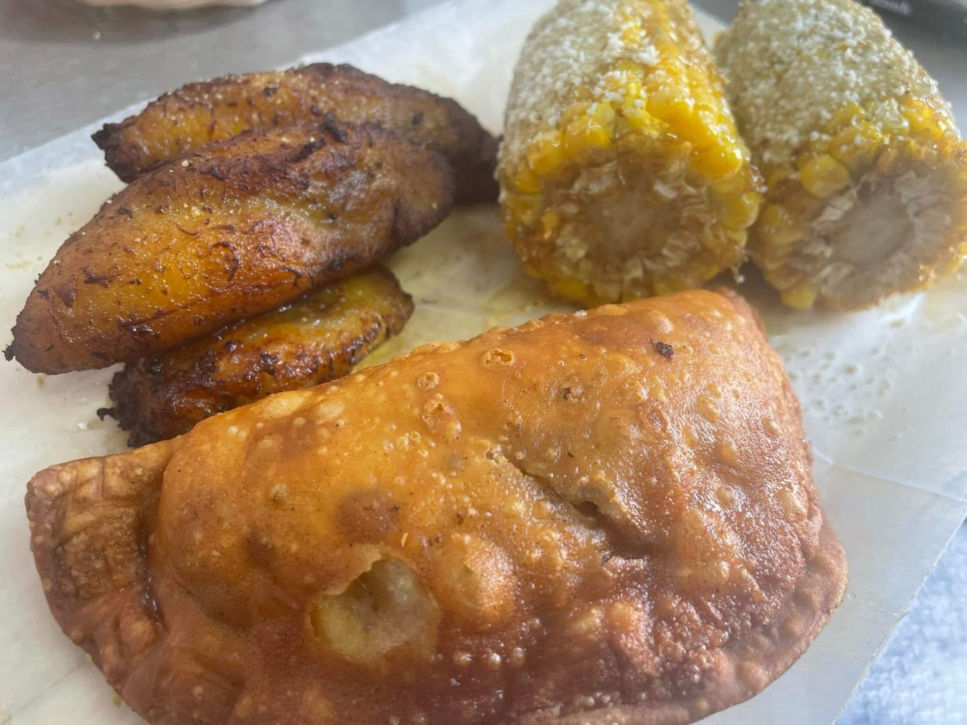 A golden empanada with fried plantains and corn on the cob